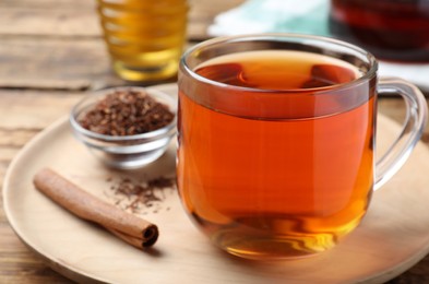Photo of Freshly brewed rooibos tea, dry leaves and cinnamon stick on wooden table, closeup
