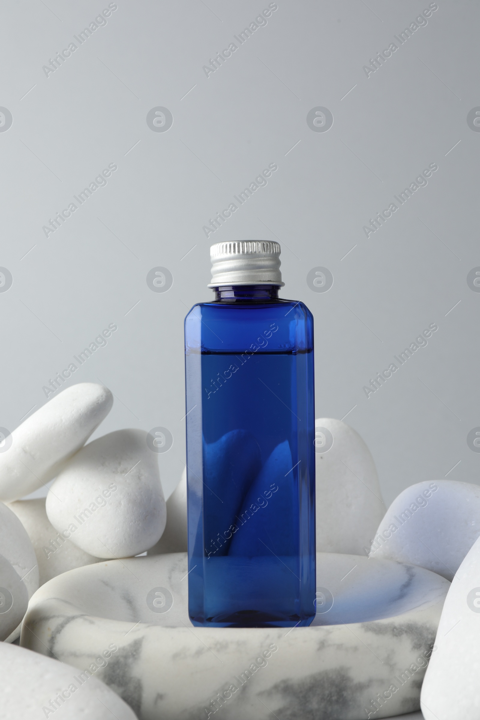 Photo of Bottle of cosmetic product and stones on light grey background