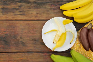 Photo of Many different bananas on wooden table, flat lay. Space for text