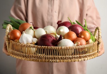 Photo of Woman holding tray with fresh onions and garlic on light background, closeup