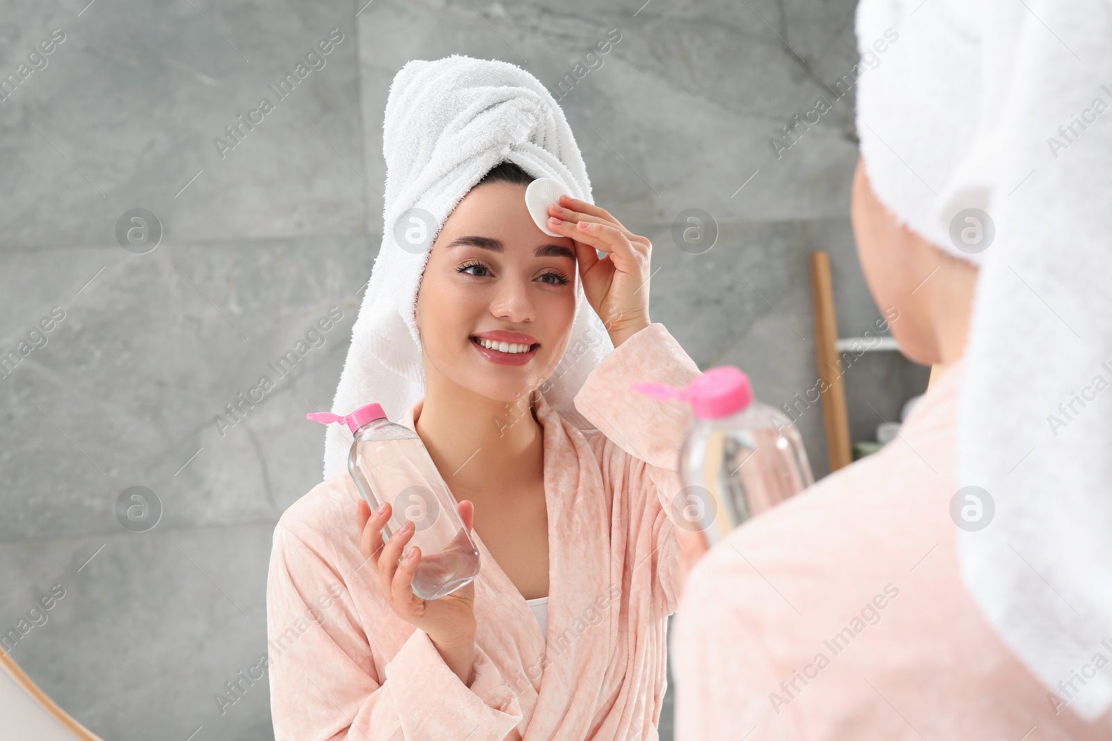 Photo of Beautiful woman in terry towel removing makeup with cotton pad near mirror indoors