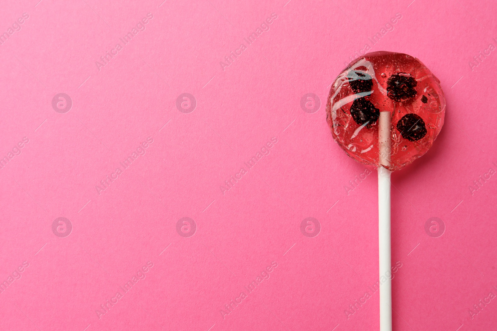 Photo of Sweet colorful lollipop with berries on pink background, top view. Space for text