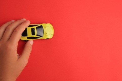 Child playing with toy car on red background, top view. Space for text