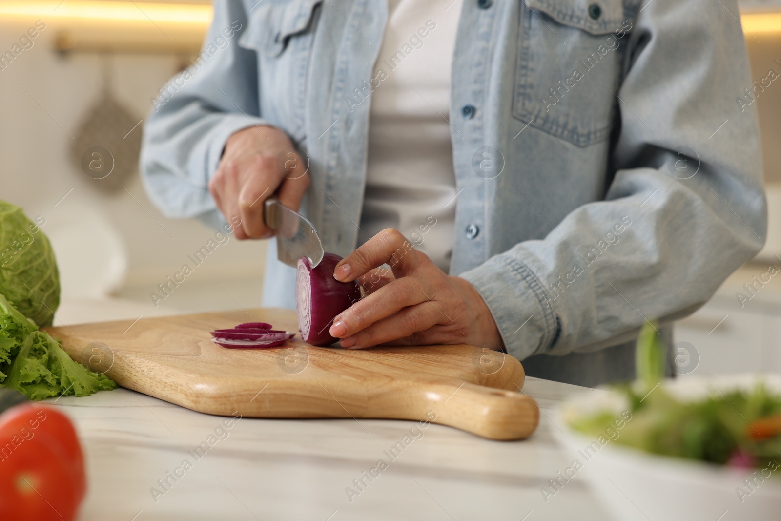 Photo of Woman cutting onion at white marble table in kitchen, closeup