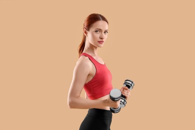 Photo of Young woman in sportswear doing exercises with dumbbells on beige background