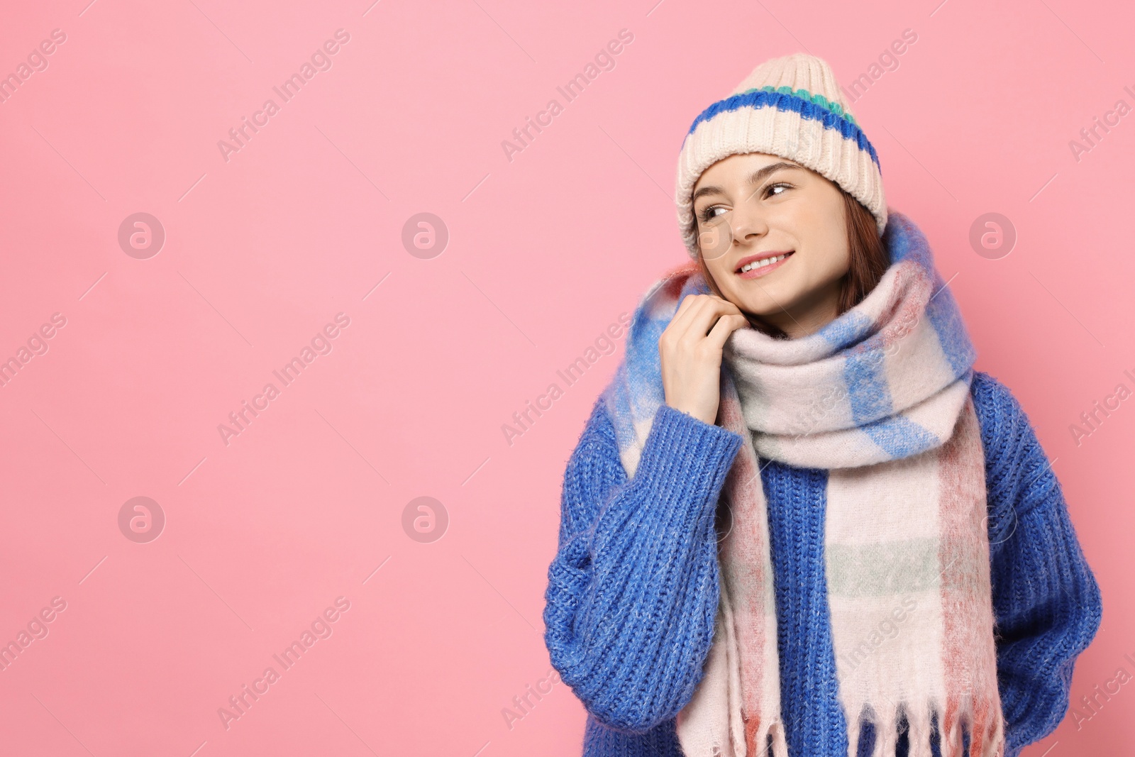 Photo of Beautiful woman in warm scarf and hat on pink background, space for text