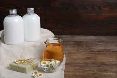 Photo of Composition with chamomile flowers and cosmetic products on wooden table, space for text