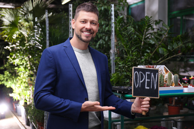 Male business owner holding OPEN sign in his flower shop