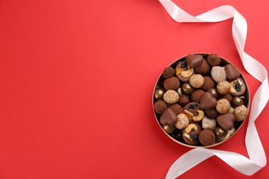 Photo of Different delicious chocolate candies in box and ribbon on red background, top view. Space for text