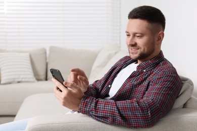 Photo of Man sending message via smartphone on sofa at home. Space for text