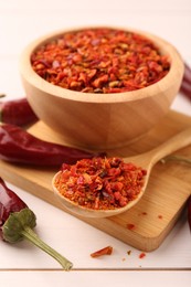 Photo of Chili pepper flakes and pods on white wooden table, closeup