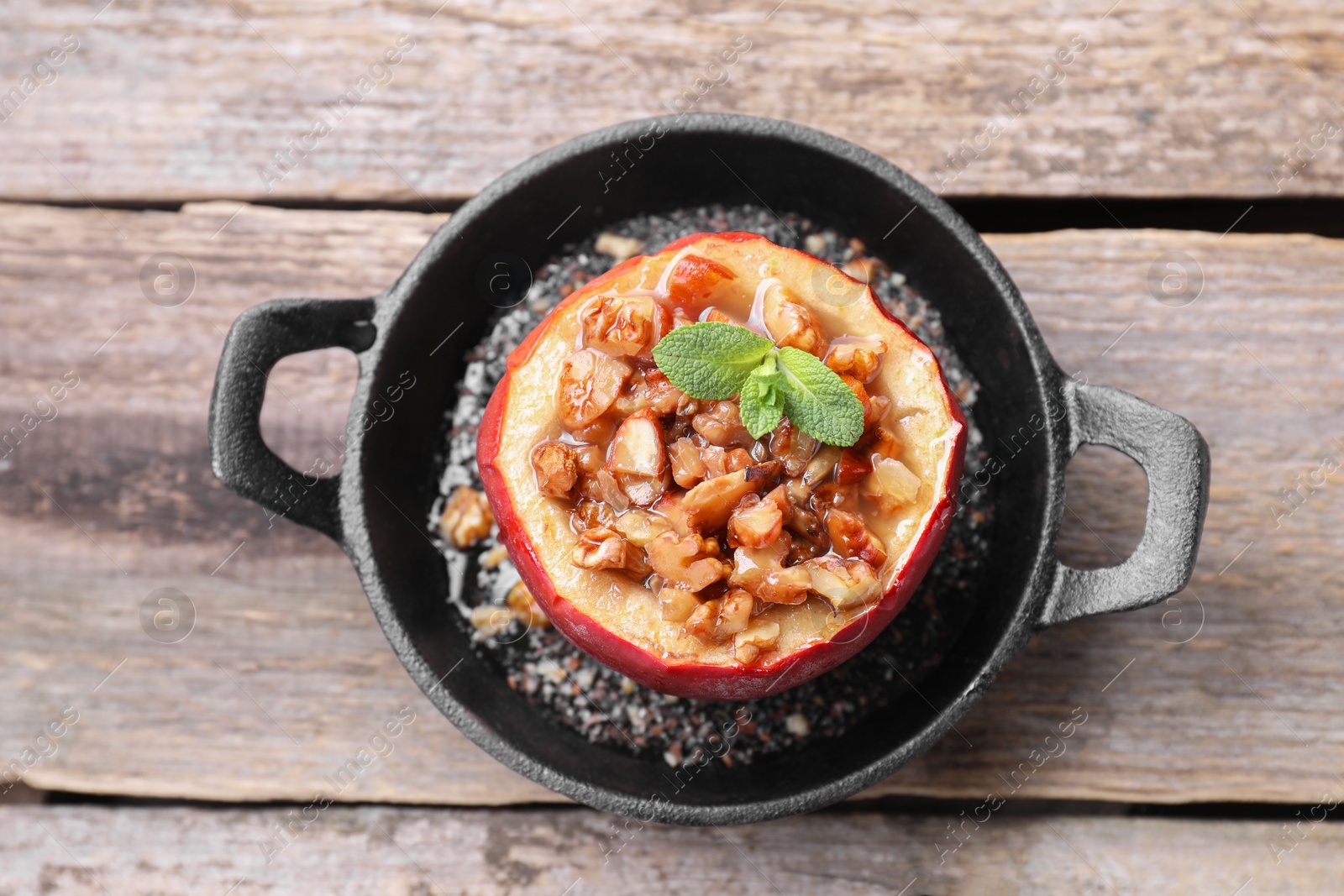 Photo of Tasty baked apple with nuts, honey and mint in baking dish on wooden table, top view