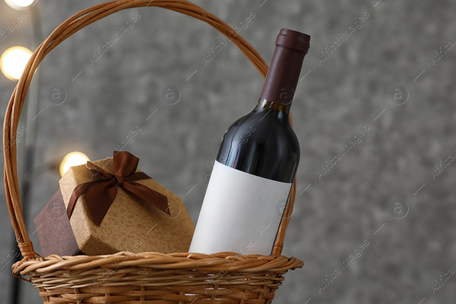 Photo of Wicker basket with bottle of wine and gift box on table. Space for design