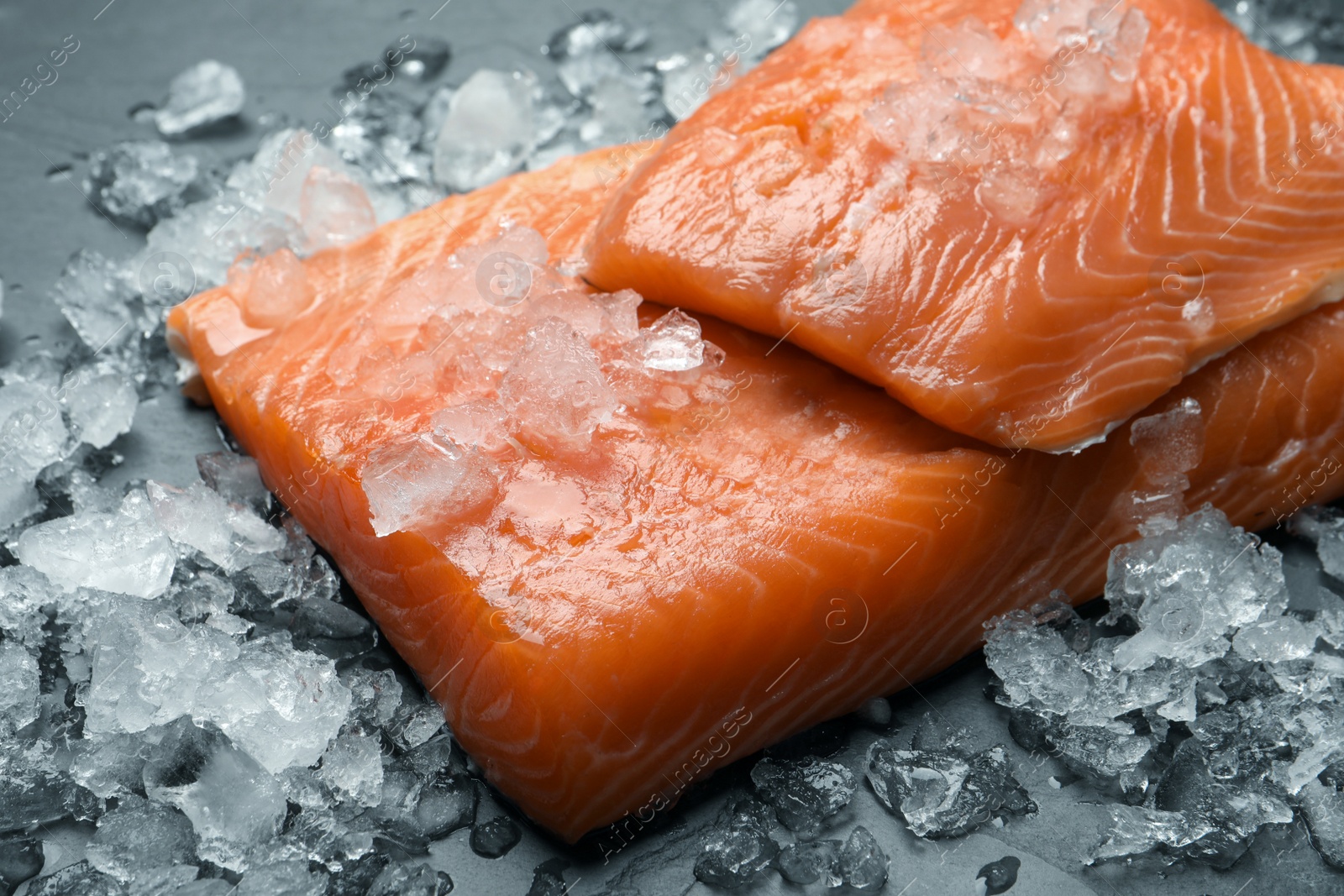 Photo of Fresh raw salmon with ice on black table, closeup