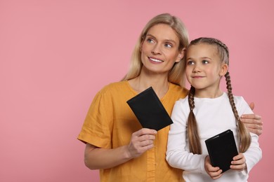 Immigration. Happy woman and her daughter with passports on pink background, space for text