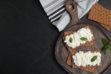 Crispy crackers with cottage cheese and basil on black table, flat lay. Space for text