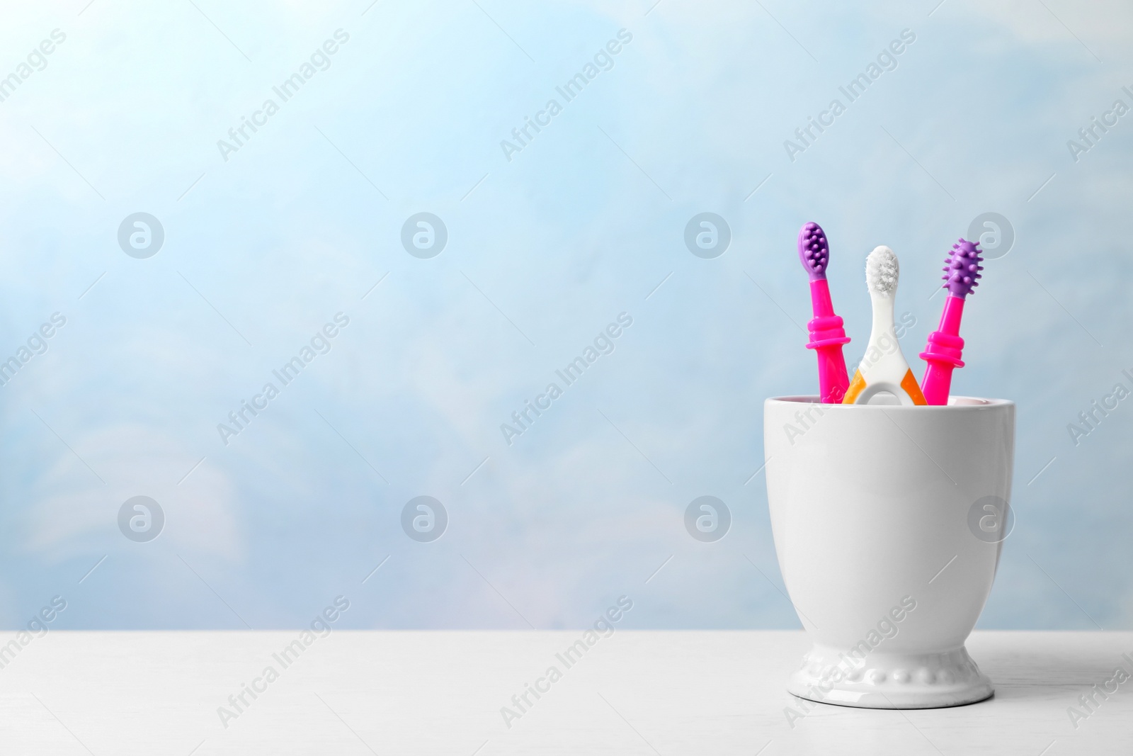 Photo of Baby toothbrushes in holder on table against color background with space for text