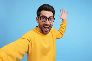 Photo of Happy man taking selfie on light blue background, space for text