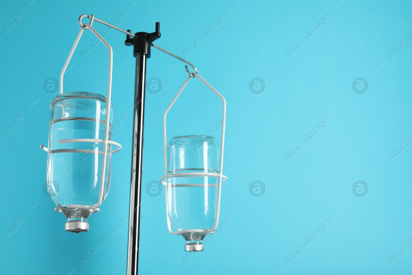 Photo of IV infusion set on pole against light blue background. Space for text