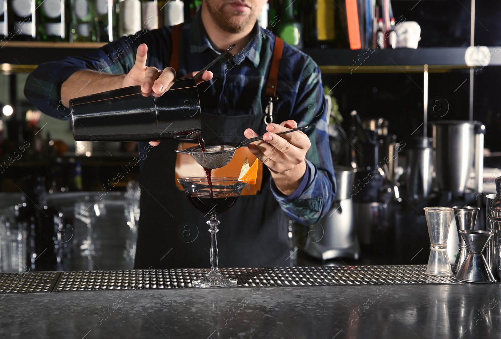 Photo of Barman pouring alcoholic cocktail into glass at counter in pub, closeup