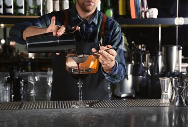Photo of Barman pouring alcoholic cocktail into glass at counter in pub, closeup
