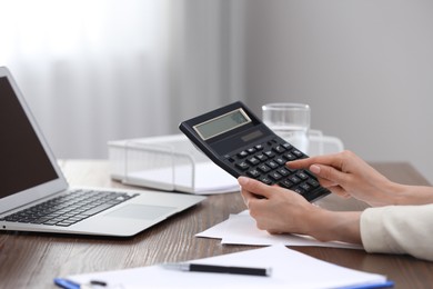 Photo of Woman using calculator at table indoors, closeup