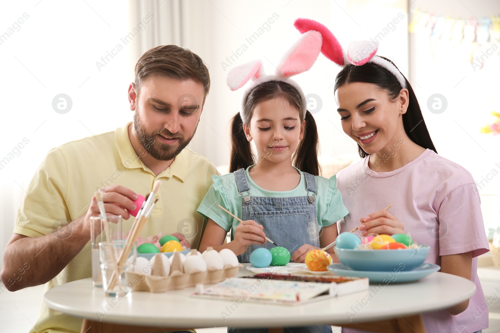 Photo of Happy family painting Easter eggs at table indoors