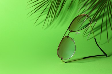 Photo of Stylish sunglasses and palm branches on green background. Space for text