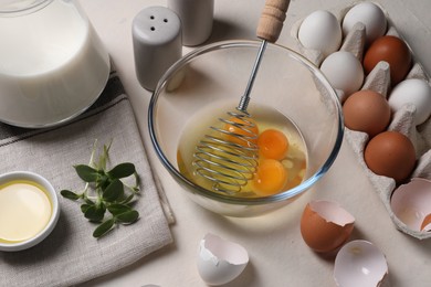 Photo of Metal whisk, raw eggs in bowl and ingredients on light table