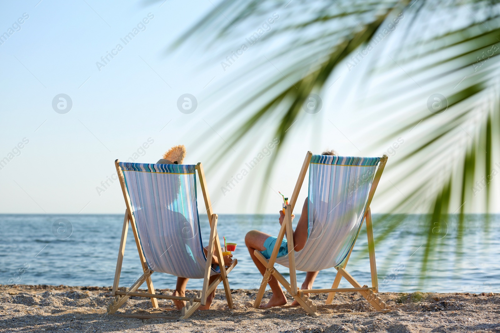 Photo of Young couple with cocktails in beach chairs at seacoast