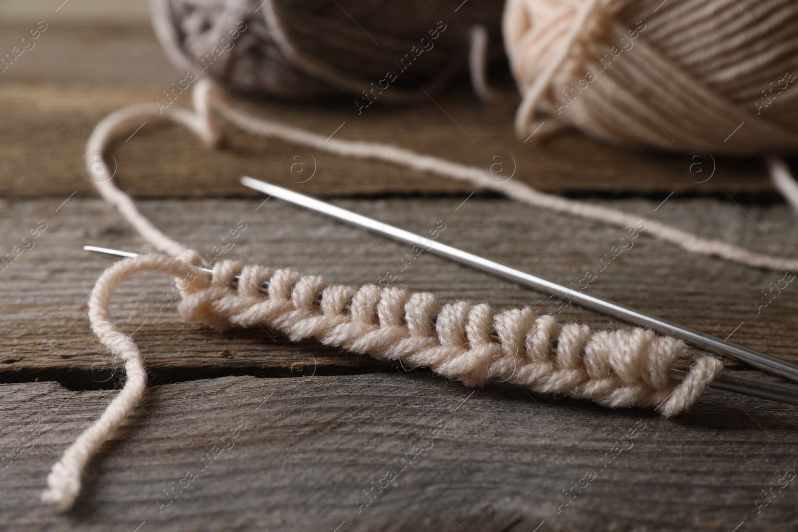 Photo of Soft beige knitting and metal needles on wooden table, closeup