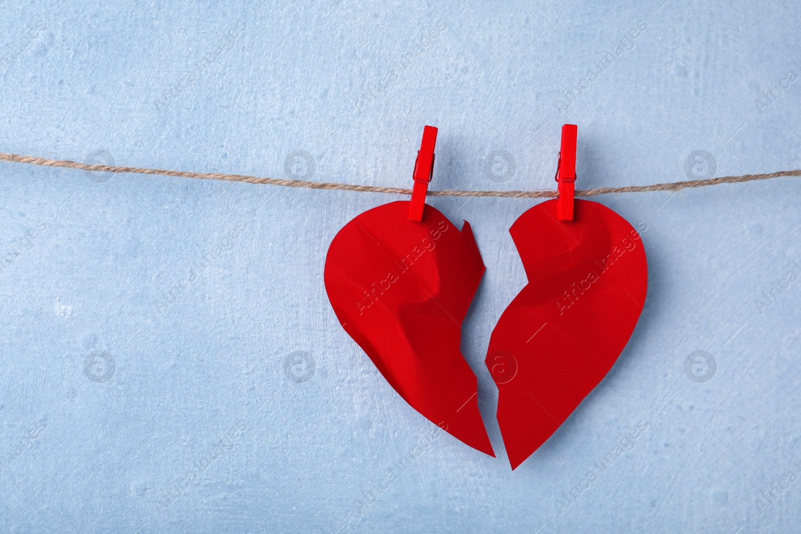 Photo of Halves of torn paper heart pinned on laundry string near light wall, space for text. Relationship problems concept