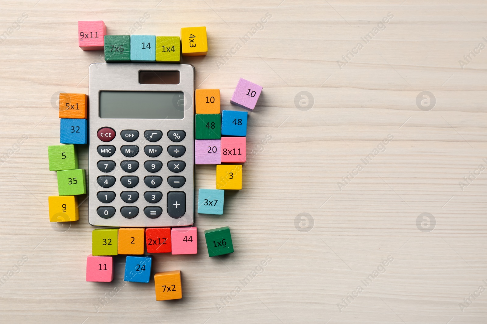 Photo of Colorful cubes with numbers and multiplications near calculator on white wooden table, flat lay. Space for text