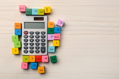 Photo of Colorful cubes with numbers and multiplications near calculator on white wooden table, flat lay. Space for text