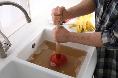 Man using plunger to unclog sink drain in kitchen, closeup