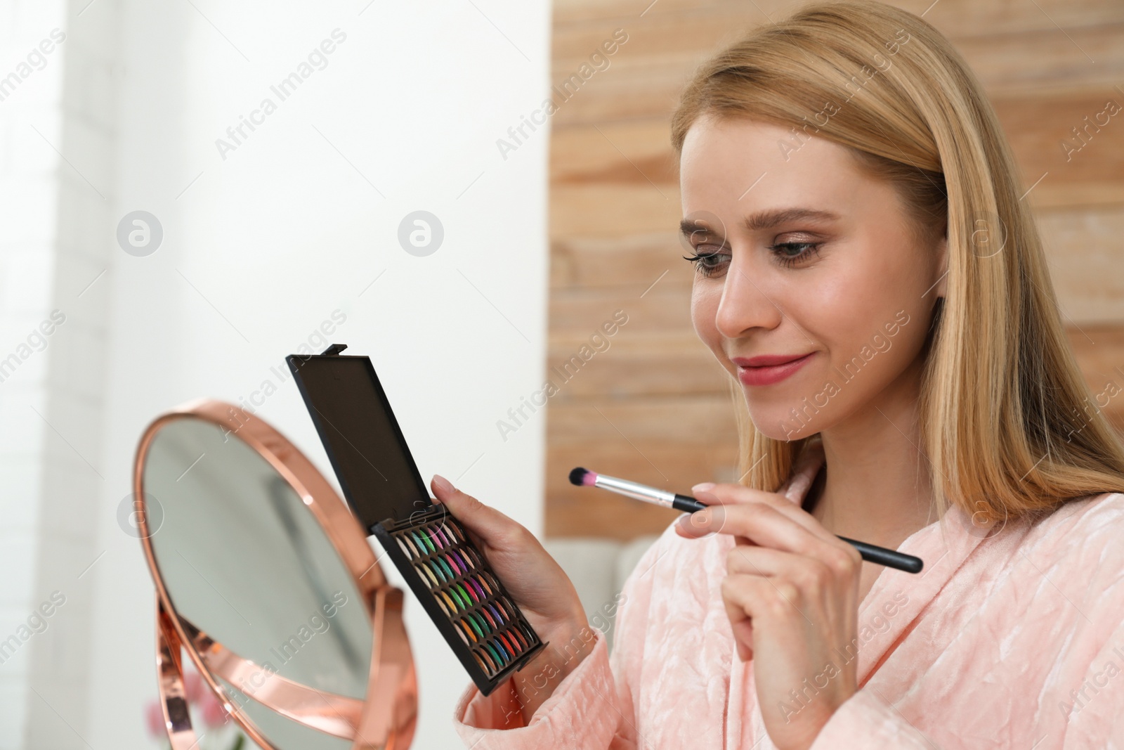 Photo of Beautiful happy woman applying makeup in room