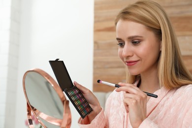 Photo of Beautiful happy woman applying makeup in room