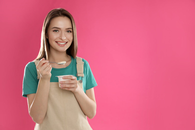 Photo of Young attractive woman with tasty yogurt on pink background. Space for text