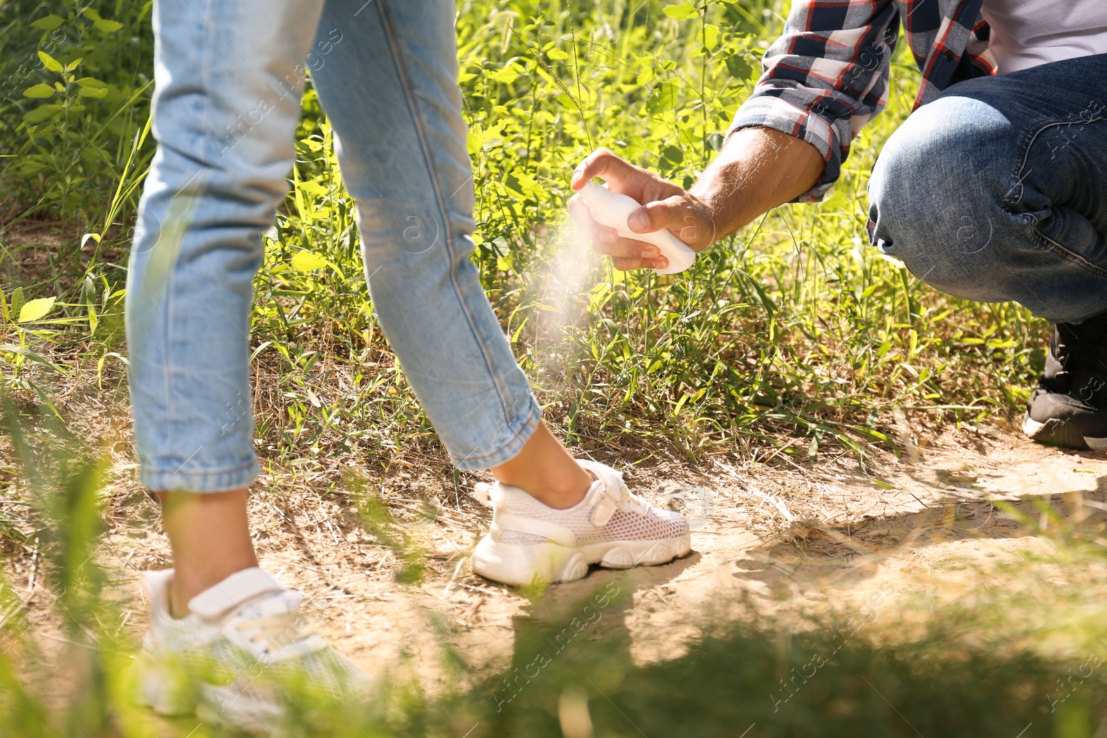 Photo of Father spraying tick repellent on his little daughter's leg during hike in nature, closeup