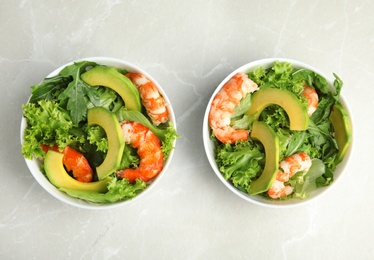 Delicious avocado salad with shrimps in bowls on grey marble table, flat lay