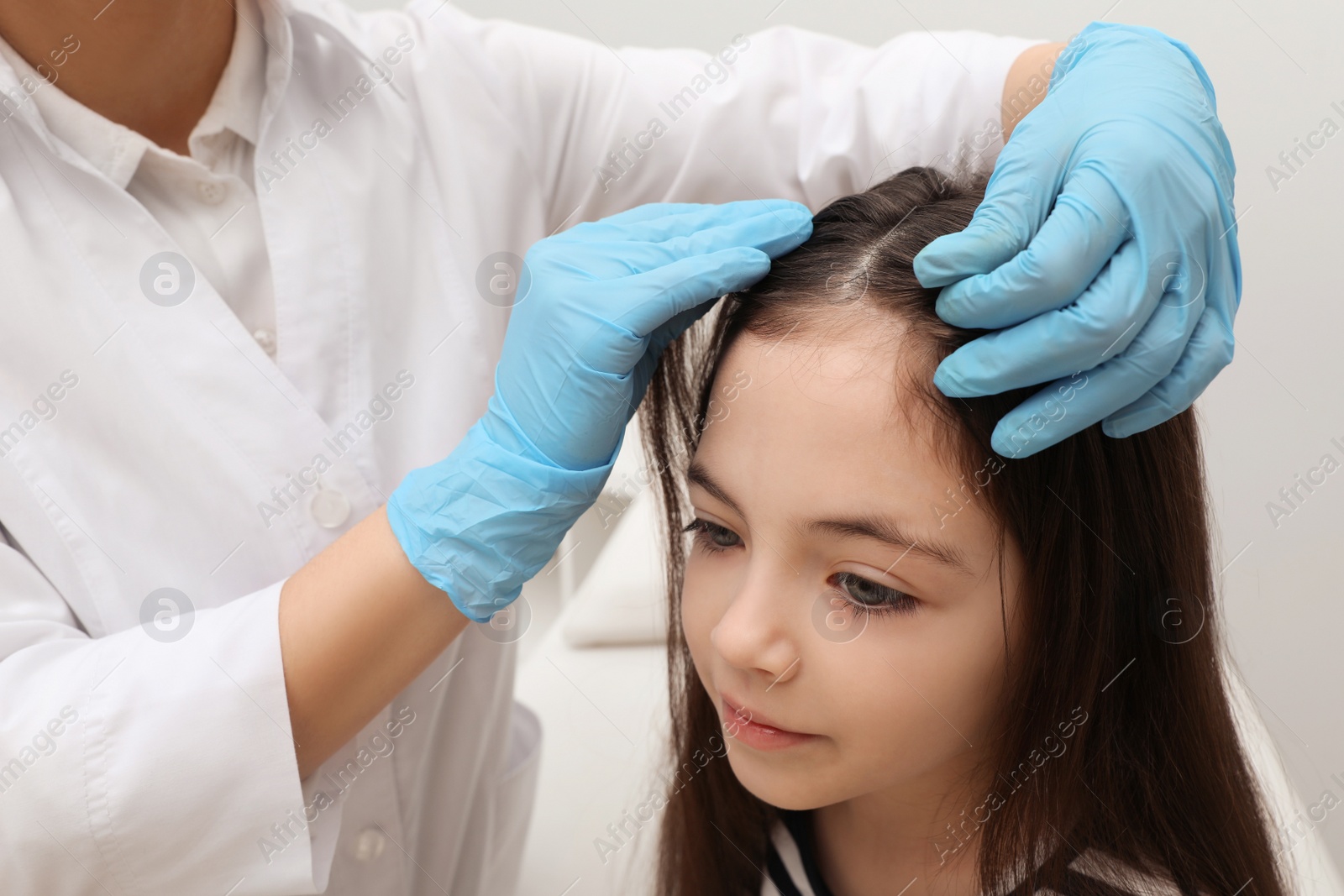 Photo of Doctor examining little girl's hair indoors. Anti lice treatment