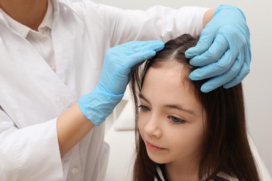 Photo of Doctor examining little girl's hair indoors. Anti lice treatment