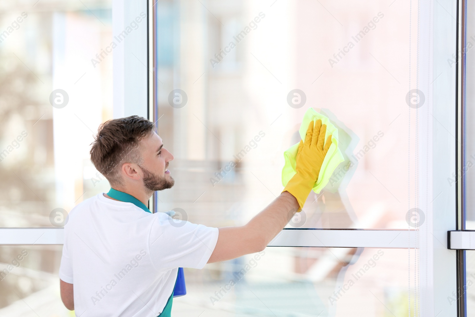 Photo of Young man cleaning window with rag indoors