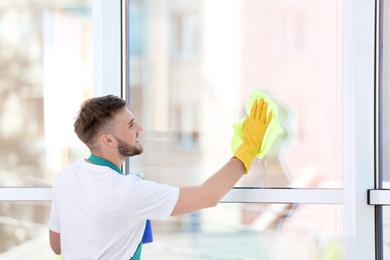 Photo of Young man cleaning window with rag indoors