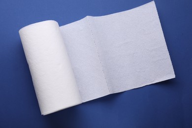 Photo of Roll of tissue towels on blue background, top view