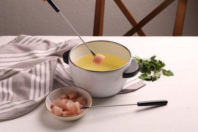 Photo of Dipping piece of raw meat into oil in fondue pot at white wooden table