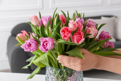 Photo of Woman putting bouquet of beautiful tulips in vase indoors, closeup