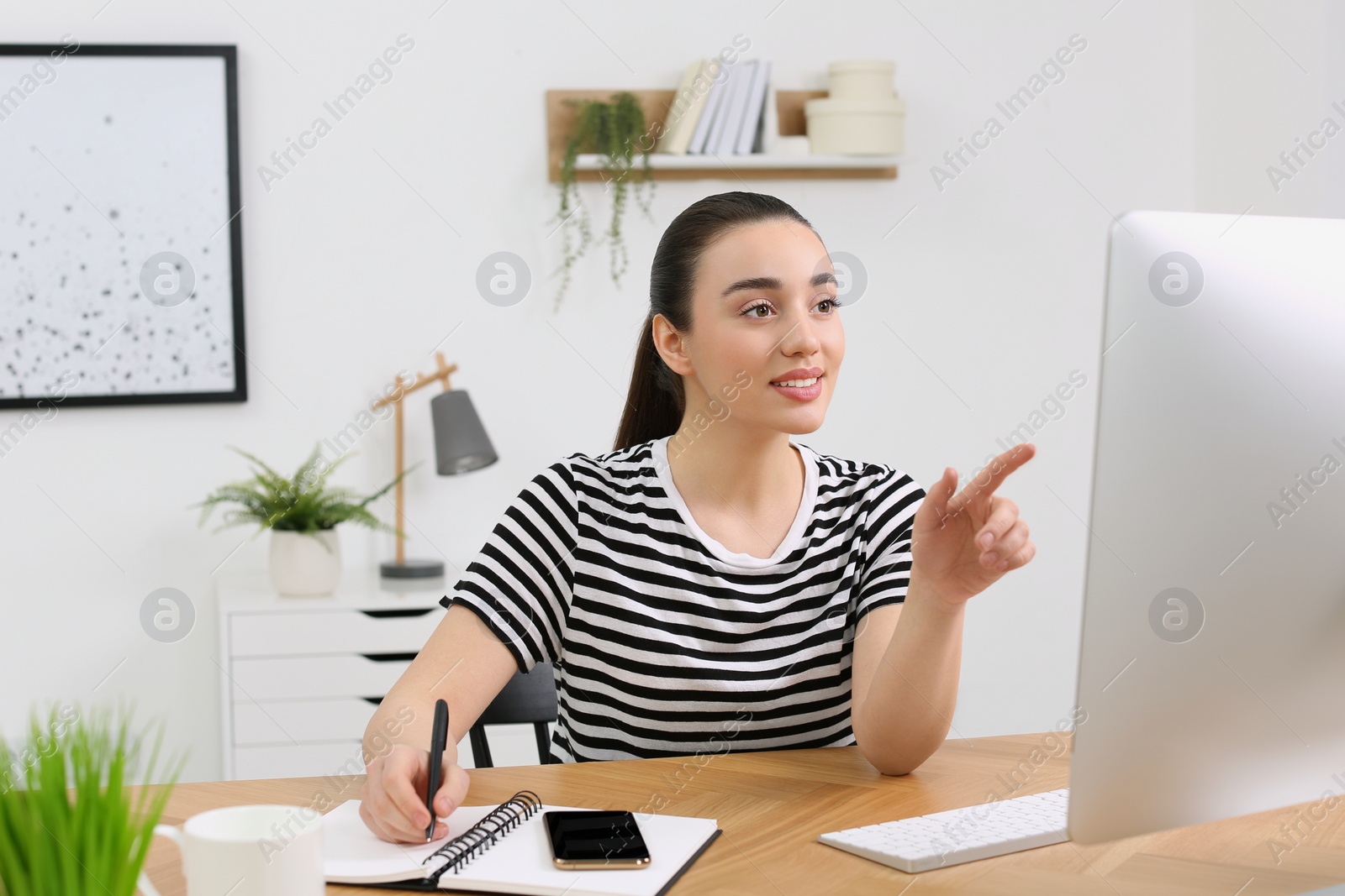 Photo of Home workplace. Happy woman working on computer at wooden desk in room