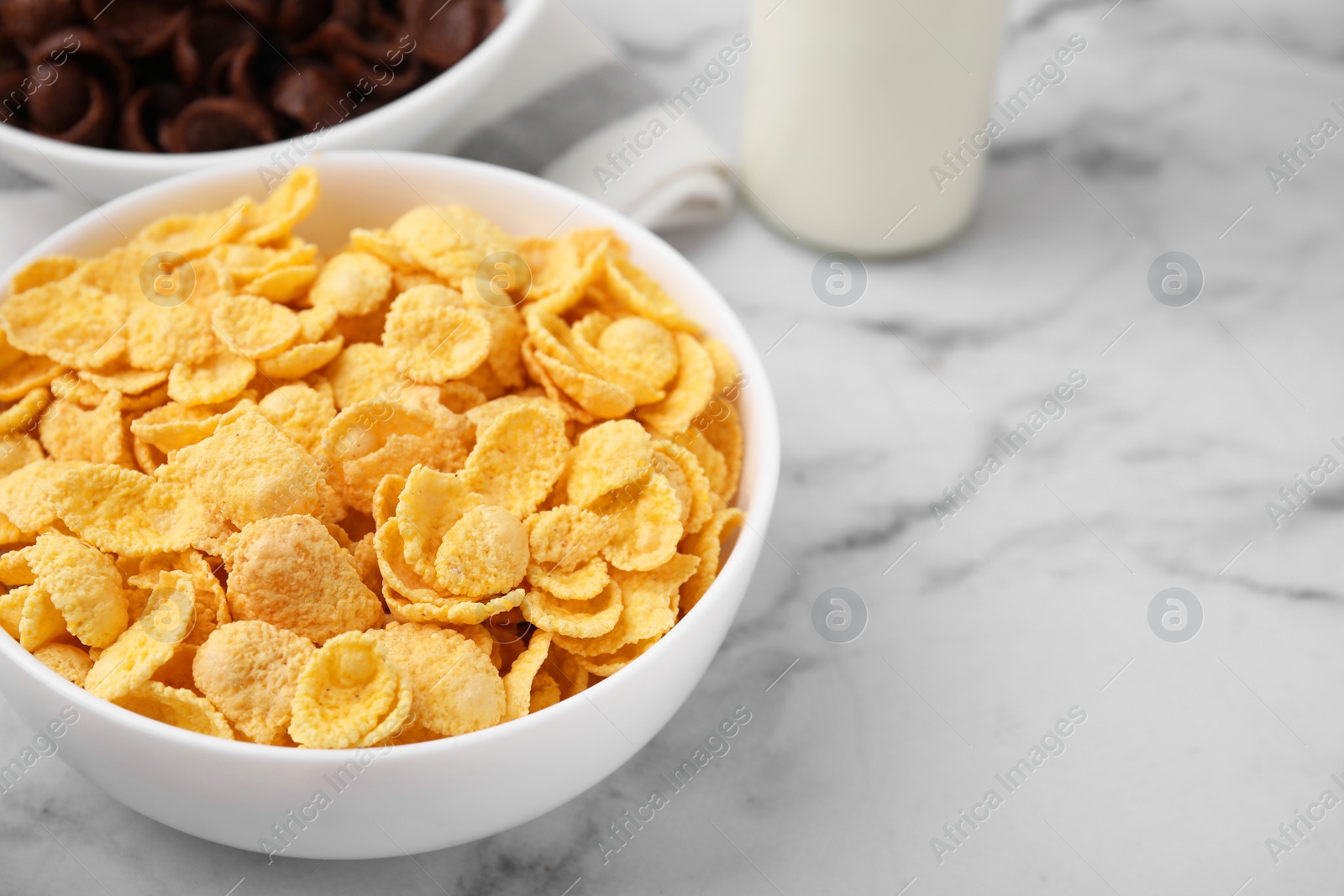 Photo of Breakfast cereal. Tasty crispy corn flakes in bowls on white marble table, closeup. Space for text