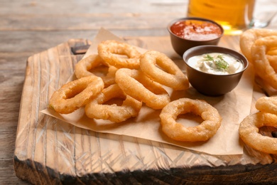 Photo of Fried onion rings served with sauces on wooden board, closeup